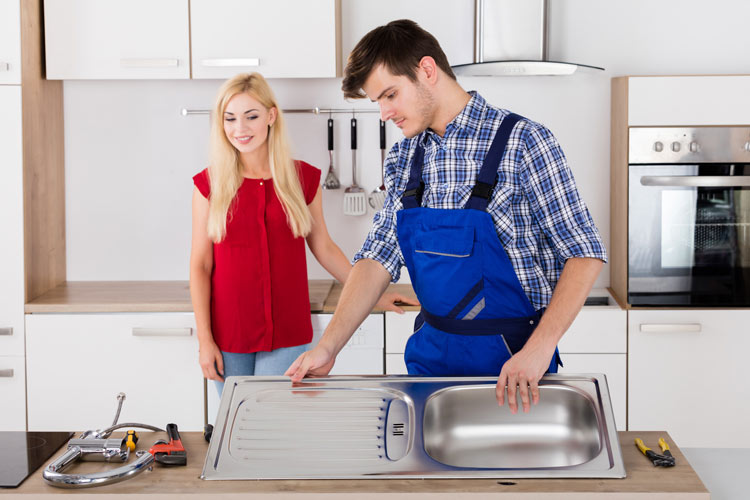 man installing stainless steel sink in home woman homeowner standing near